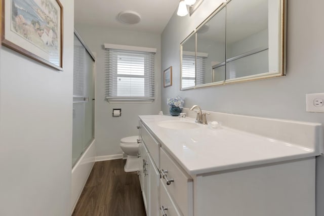 bathroom with combined bath / shower with glass door, baseboards, toilet, wood finished floors, and vanity