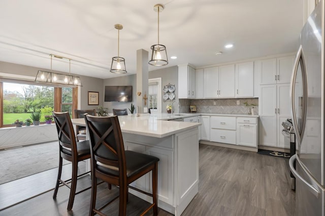 kitchen featuring a kitchen bar, a peninsula, freestanding refrigerator, and white cabinetry