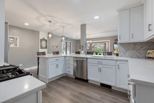 kitchen with stainless steel dishwasher, decorative light fixtures, a sink, white cabinetry, and a peninsula
