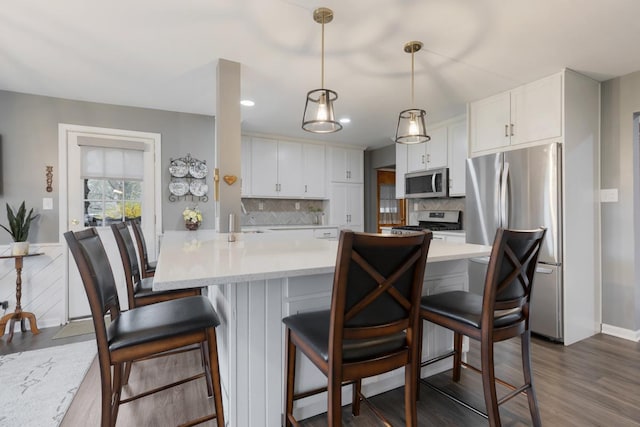 kitchen with dark wood finished floors, stainless steel appliances, light countertops, backsplash, and white cabinetry