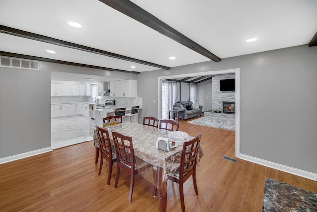 127 Tottenham Ln, Elk Grove Village, IL 60007 - dining space featuring light wood-style flooring, a fireplace, baseboards, visible vents, and beam ceiling