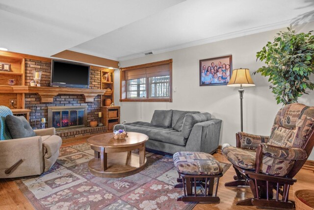 living room featuring crown molding, built in features, wood finished floors, and a fireplace