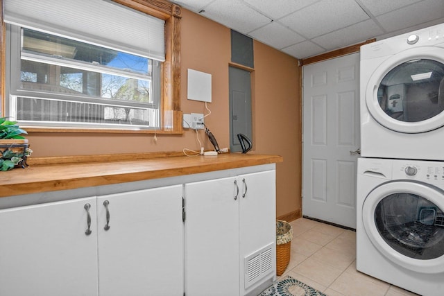 clothes washing area with stacked washing maching and dryer, light tile patterned floors, cabinet space, and visible vents
