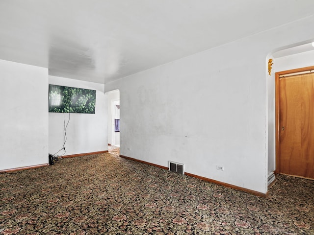 carpeted spare room featuring baseboards, visible vents, and arched walkways