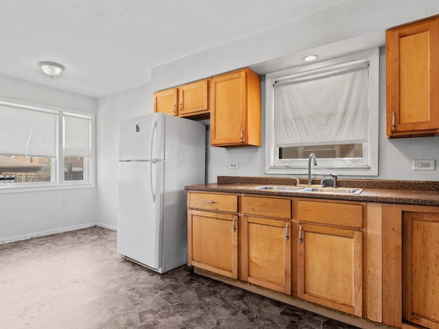 kitchen with baseboards, a sink, dark countertops, freestanding refrigerator, and brown cabinetry