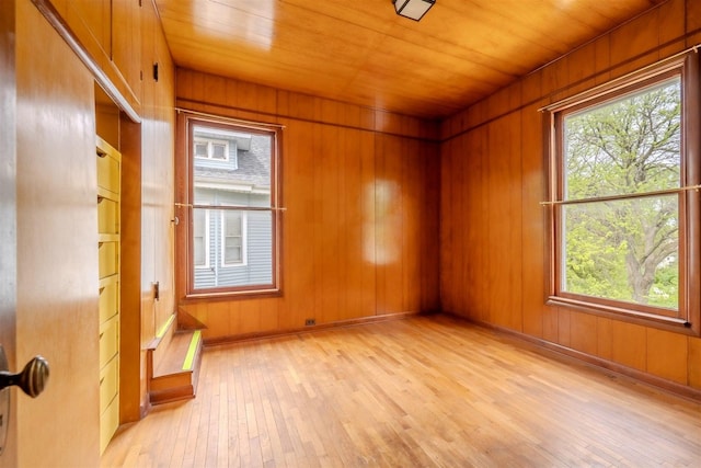 empty room with light wood-type flooring, wood ceiling, and wooden walls