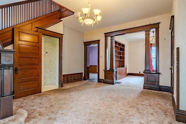 unfurnished room featuring carpet flooring, ornate columns, and a chandelier