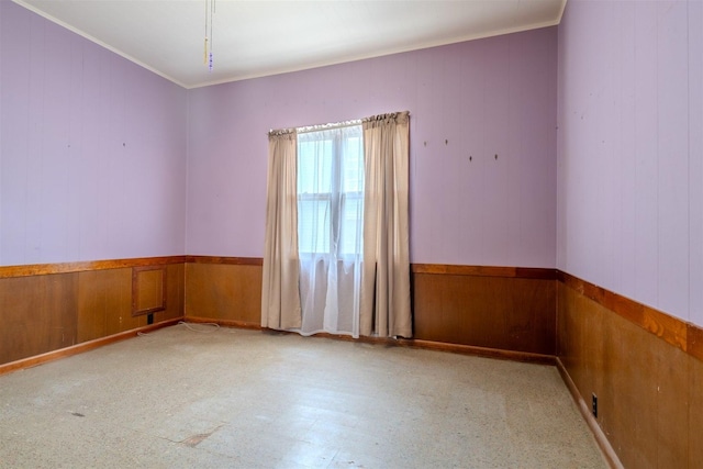 unfurnished room with a wainscoted wall, wood walls, tile patterned floors, and ornamental molding