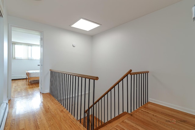 stairs with a baseboard radiator, wood finished floors, and baseboards