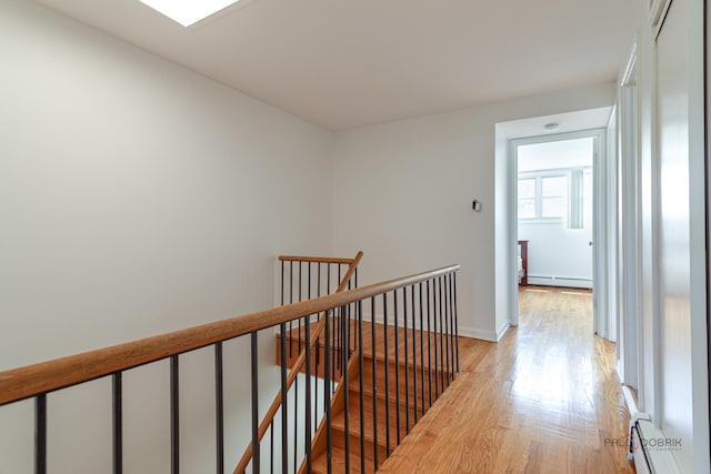 corridor featuring an upstairs landing, light wood-style flooring, baseboards, baseboard heating, and a baseboard heating unit