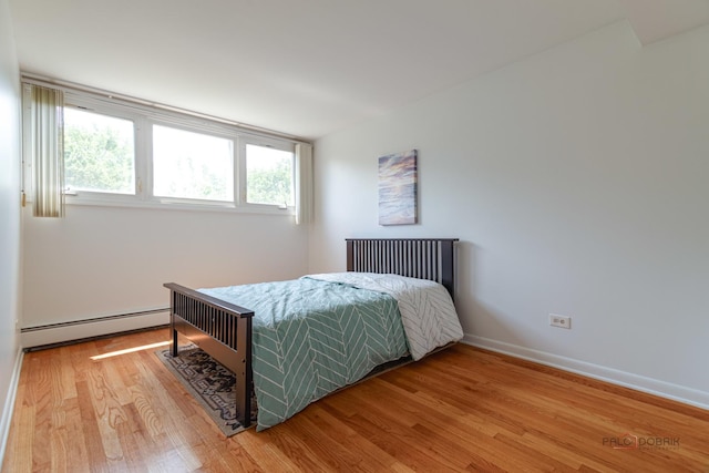 bedroom with wood finished floors, baseboards, and baseboard heating