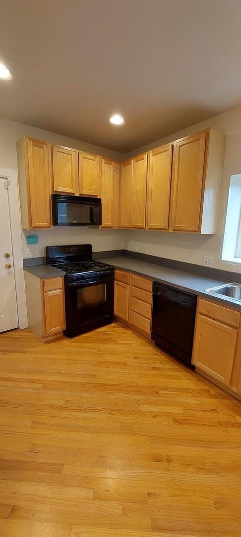 kitchen with light wood-style flooring, a sink, light brown cabinets, and black appliances