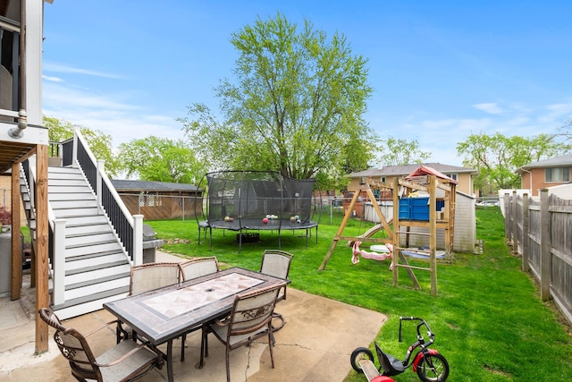 view of patio / terrace featuring outdoor dining area, a trampoline, stairway, a fenced backyard, and a playground