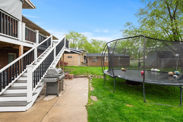 view of yard with a trampoline, a wooden deck, stairway, fence, and a patio