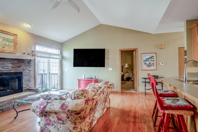 living area with ceiling fan, light wood-style flooring, vaulted ceiling, and a stone fireplace