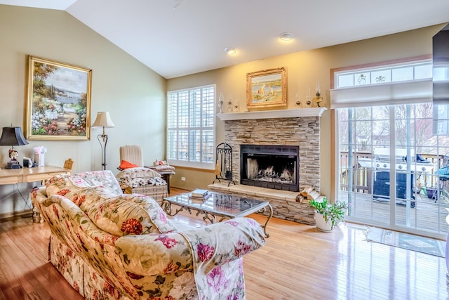 living room featuring a stone fireplace, baseboards, vaulted ceiling, and wood finished floors