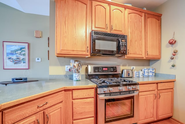 kitchen with black microwave, light countertops, stainless steel gas range, and light brown cabinets