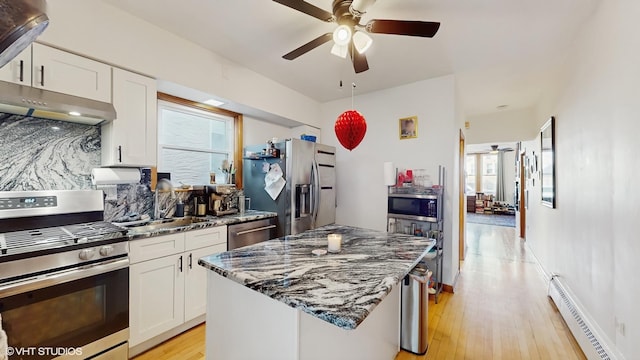 kitchen featuring ceiling fan, stainless steel appliances, dark stone counters, baseboard heating, and tasteful backsplash