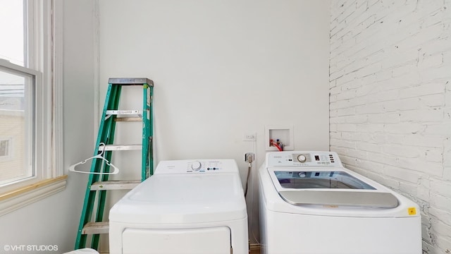 laundry area featuring separate washer and dryer, brick wall, laundry area, and a wealth of natural light