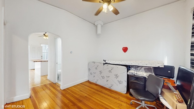 home office featuring arched walkways, ceiling fan, baseboards, and hardwood / wood-style flooring