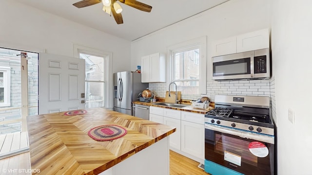 kitchen with stainless steel appliances, butcher block counters, white cabinetry, a sink, and backsplash