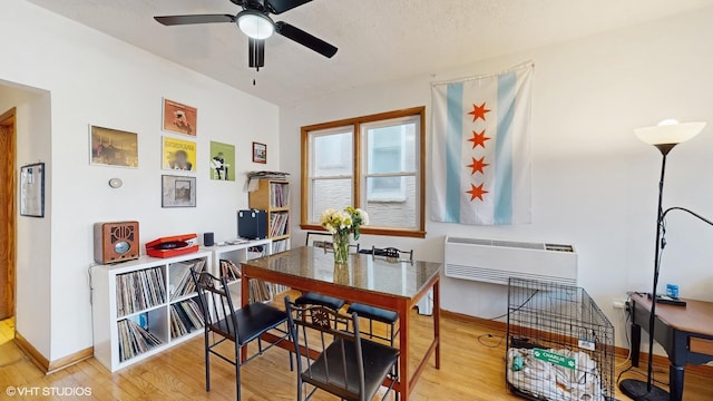 dining area featuring baseboards, wood finished floors, an AC wall unit, and a ceiling fan