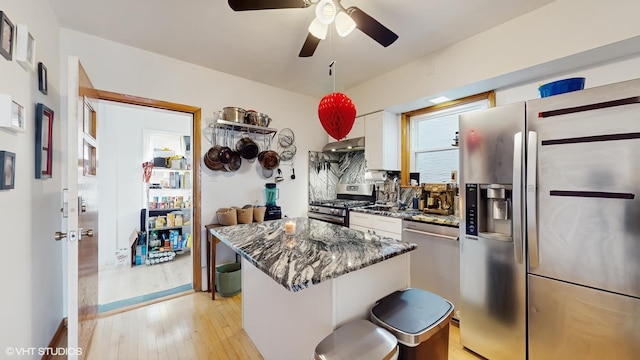 kitchen featuring range hood, dark stone countertops, stainless steel appliances, white cabinets, and ceiling fan