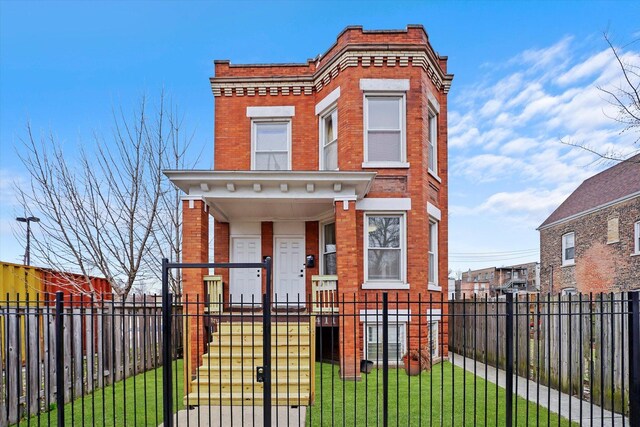 view of front of home with brick siding, a porch, a fenced front yard, and a front lawn