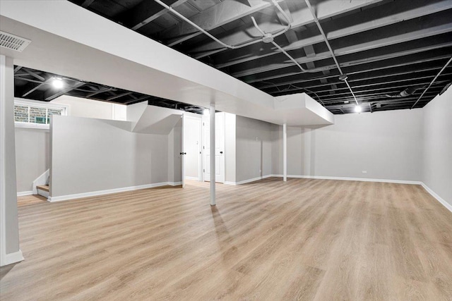 below grade area featuring baseboards, visible vents, light wood-style flooring, and stairs
