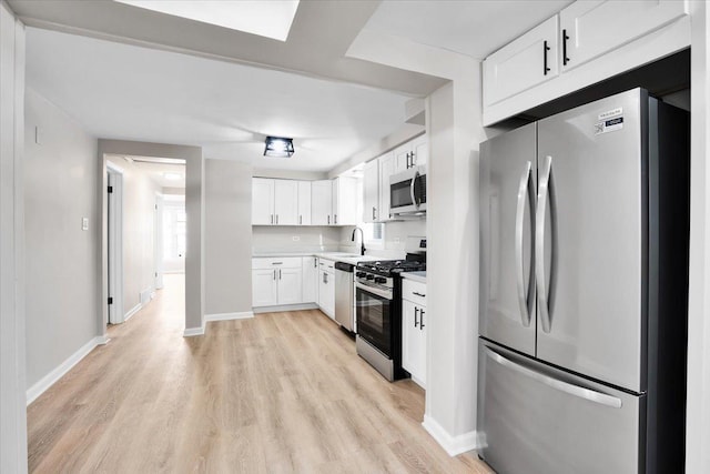 kitchen featuring light countertops, light wood-style flooring, stainless steel appliances, white cabinetry, and a sink