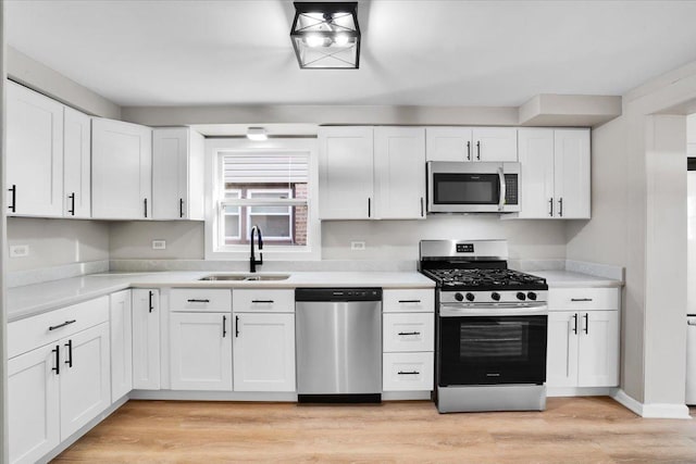 kitchen featuring light countertops, a sink, light wood-type flooring, stainless steel appliances, and white cabinets