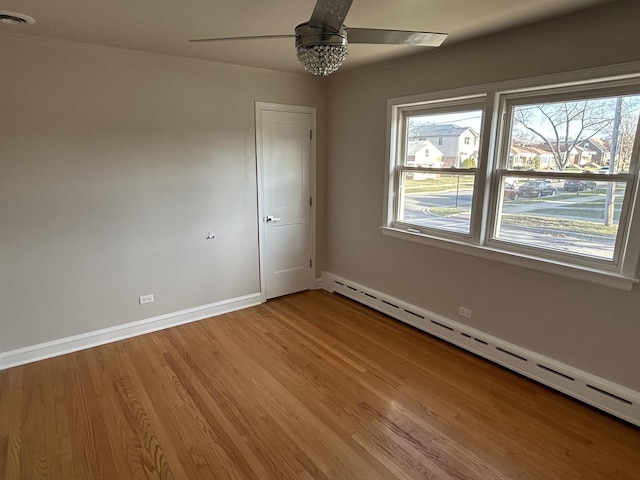empty room with plenty of natural light, baseboards, light wood-style floors, a baseboard radiator, and a ceiling fan