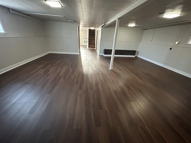 finished below grade area featuring baseboards, stairway, and dark wood finished floors