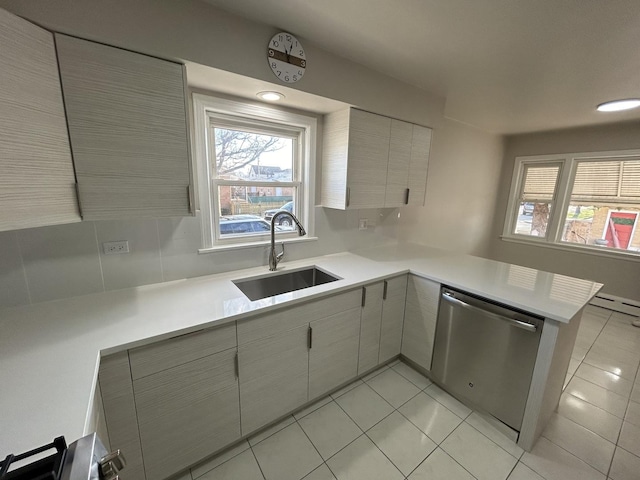 kitchen featuring light countertops, a sink, dishwasher, a peninsula, and light tile patterned floors