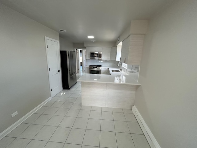 kitchen with light countertops, a peninsula, stainless steel appliances, a sink, and light tile patterned floors
