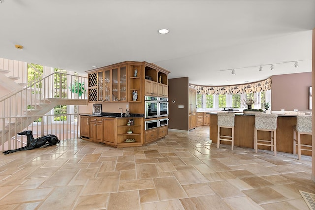 621 Chatfield Rd, New Lenox, IL 60451 - kitchen with open shelves, stainless steel oven, brown cabinetry, rail lighting, and a kitchen bar