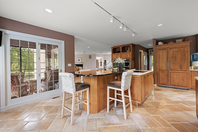 621 Chatfield Rd, New Lenox, IL 60451 - kitchen featuring rail lighting, brown cabinetry, a breakfast bar, light stone finish floors, and recessed lighting