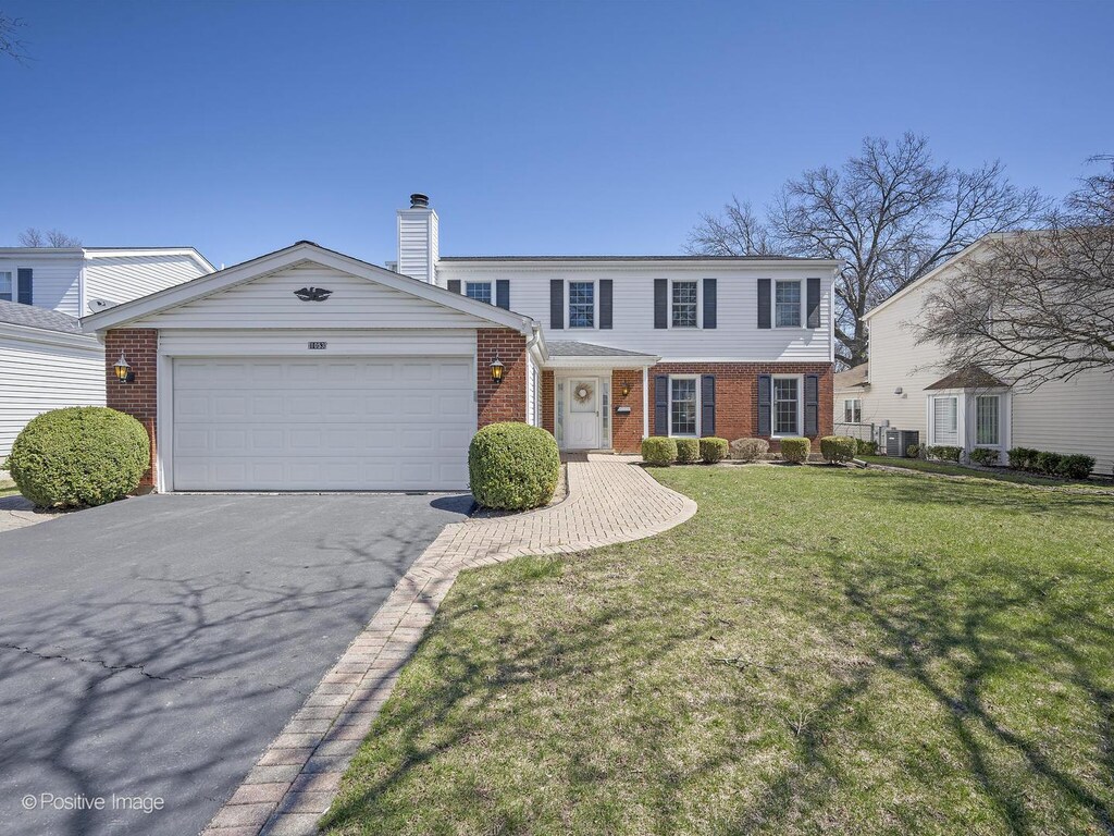 view of front of house featuring a front lawn, brick siding, an attached garage, a chimney, and driveway