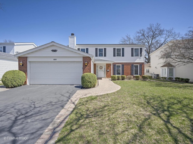 view of front of house featuring a front lawn, brick siding, an attached garage, a chimney, and driveway