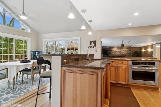 kitchen with light wood-style flooring, dark stone countertops, a sink, and stainless steel oven