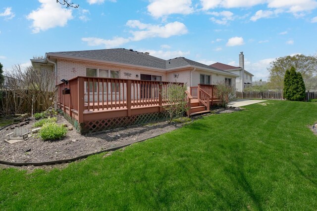 rear view of house featuring brick siding, a lawn, fence, and a wooden deck