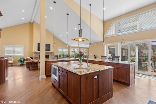 kitchen with high vaulted ceiling, a fireplace, stainless steel microwave, a sink, and open floor plan