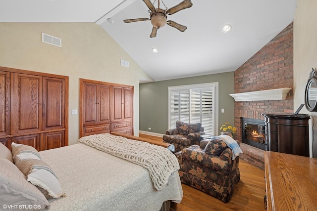 bedroom with wood finished floors, high vaulted ceiling, a fireplace, and visible vents