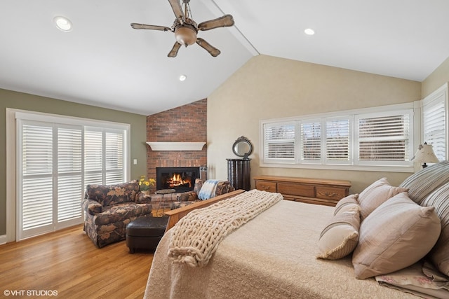bedroom featuring light wood finished floors, a brick fireplace, multiple windows, and vaulted ceiling