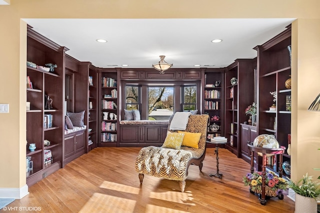 sitting room with light wood-style flooring, built in shelves, and recessed lighting