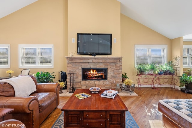 living room featuring wood finished floors, high vaulted ceiling, and a stone fireplace
