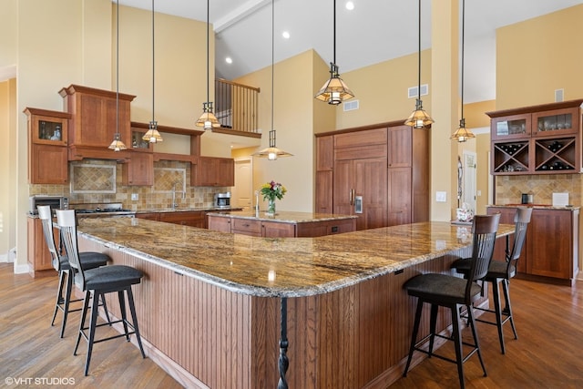 kitchen with tasteful backsplash, a high ceiling, a kitchen bar, a spacious island, and wood finished floors