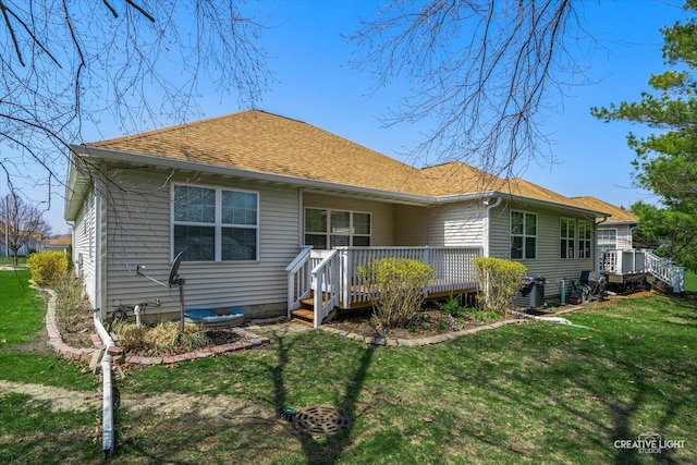 rear view of property with roof with shingles, a wooden deck, and a lawn
