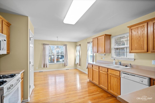 kitchen featuring white appliances, light countertops, a sink, light wood finished floors, and baseboards