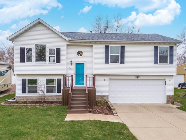 raised ranch featuring concrete driveway, a front yard, roof with shingles, and a garage